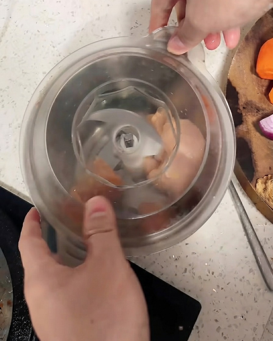 Un procesador de alimentos con la tapa asegurada sobre los trozos de pollo.