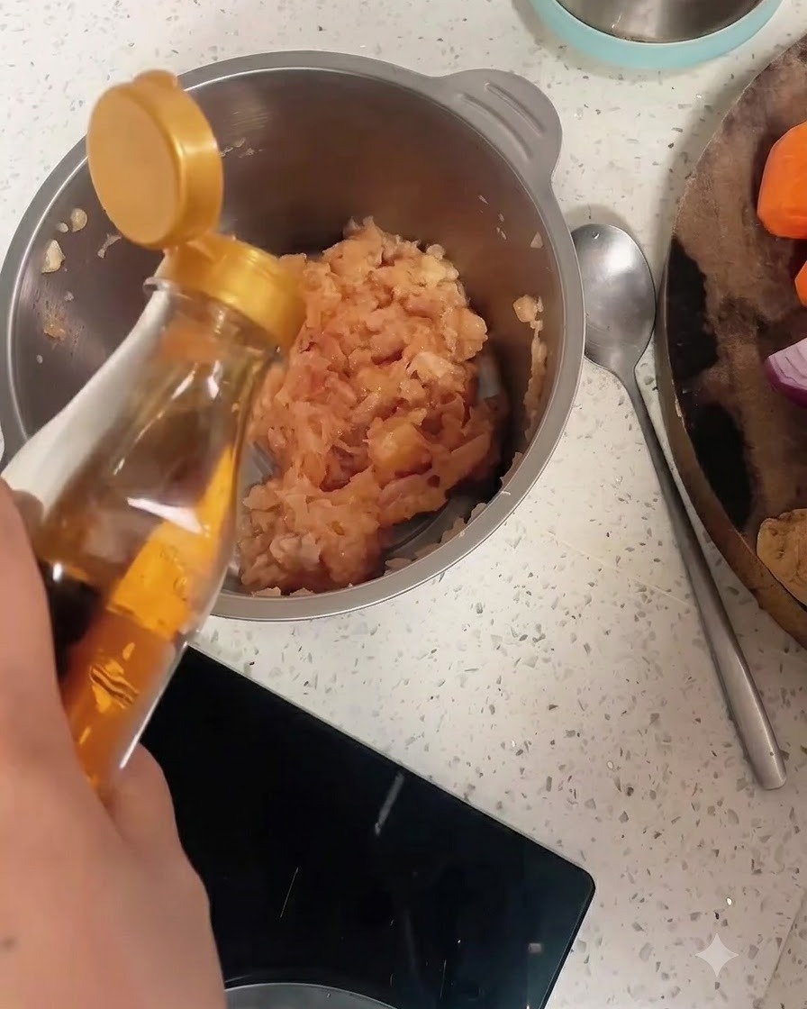Vino para cocinar siendo vertido desde una botella en un bol de acero inoxidable lleno de pollo picado y pimienta.