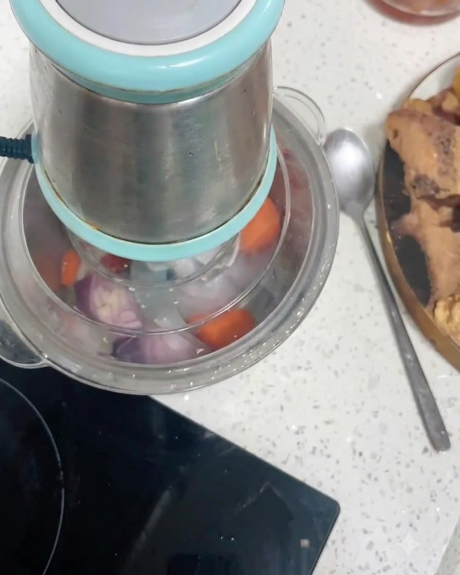Trozos de zanahoria y trozos de cebolla roja dentro del recipiente de un procesador de alimentos siendo picados.