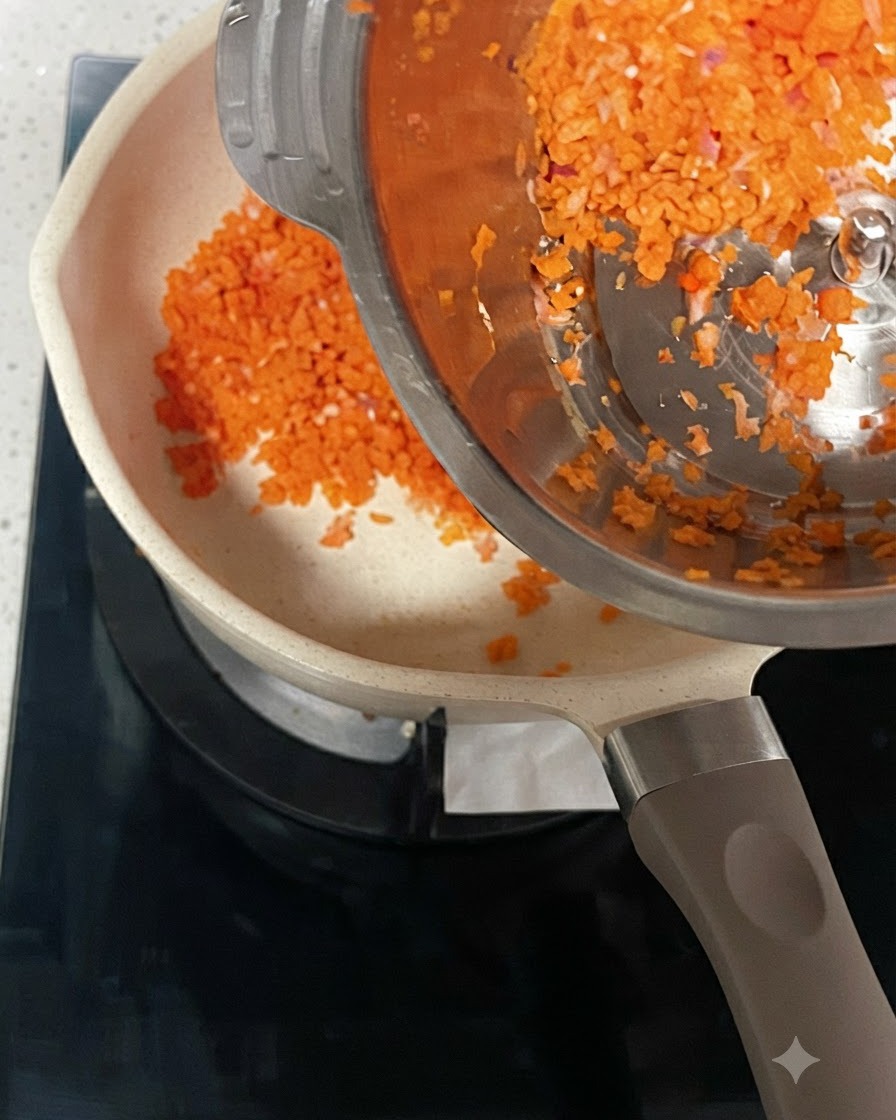 Zanahorias y cebollas picadas siendo vertidas desde un recipiente de acero en una olla caliente.