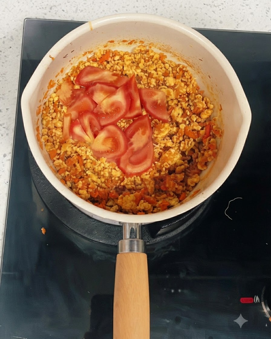 Rodajas de tomate fresco reposando sobre la mezcla cocida de pollo y verduras en una sartén.