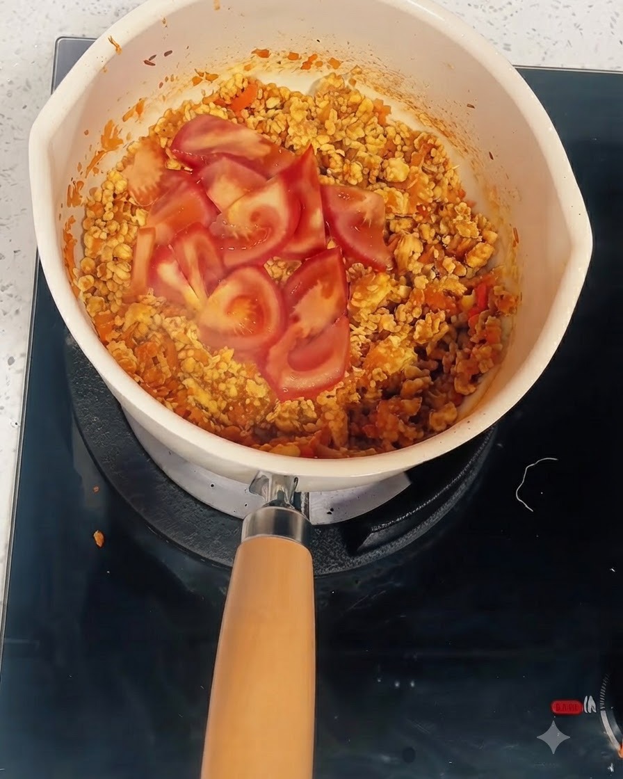 Rodajas de tomate sobre la mezcla cocida en una olla donde se agregan agua y pasta de tomate.