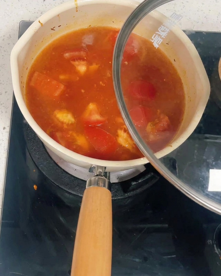 Una olla llena de salsa de tomate y pollo siendo cubierta con una tapa de vidrio.