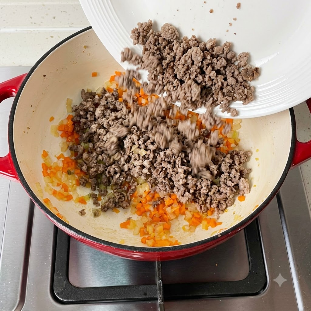 Carne picada cocida siendo añadida nuevamente a la sartén que contiene las verduras.