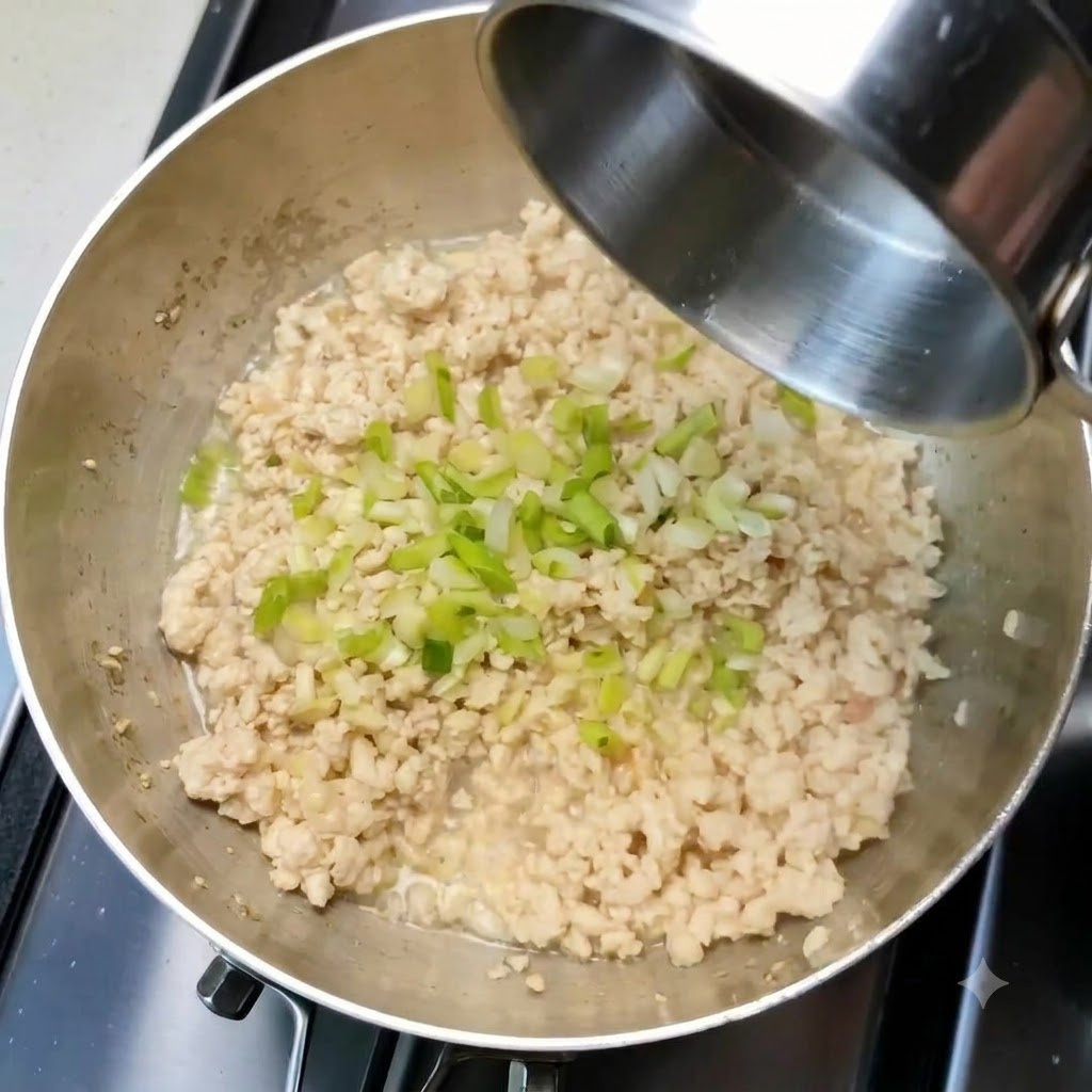 Cebollinos picados y ajo esparcidos sobre el pollo picado cocinado dentro de una sartén.