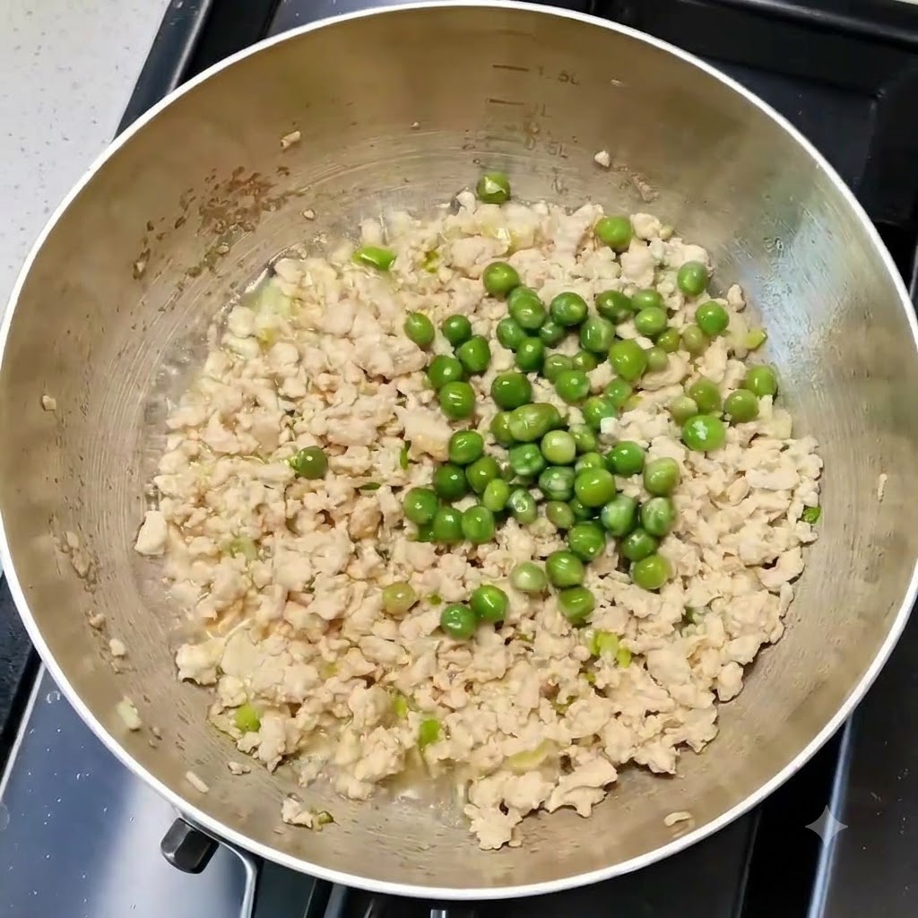 Guisantes verdes mezclados uniformemente con el pollo y los aromáticos en una sartén de cocina.