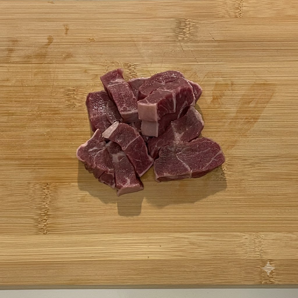 Trozos de carne de res cruda colocados en el tazón de acero de un procesador de alimentos.