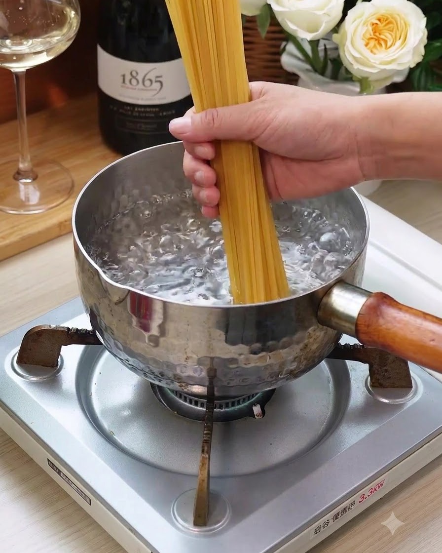 Un manojo de fideos de espagueti secos siendo sumergidos en una olla con agua hirviendo en una estufa.