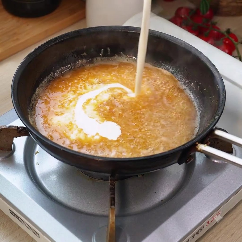 Crema espesa siendo vertida en la salsa burbujeante de la sartén, creando una mezcla envolvente.