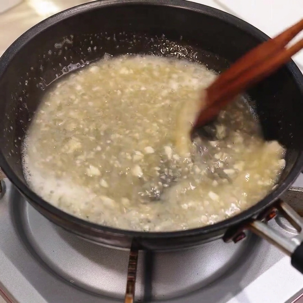 Mantequilla derritiéndose en una salsa de sartén burbujeante mientras se revuelve con palillos de madera.