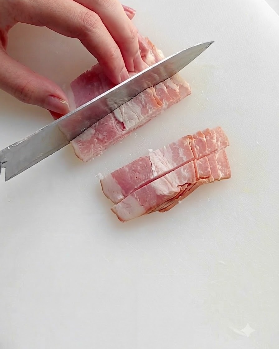 Trozos de tocino picado friéndose en una sartén caliente con aceite, mostrando grasa chispeante y bordes dorados.