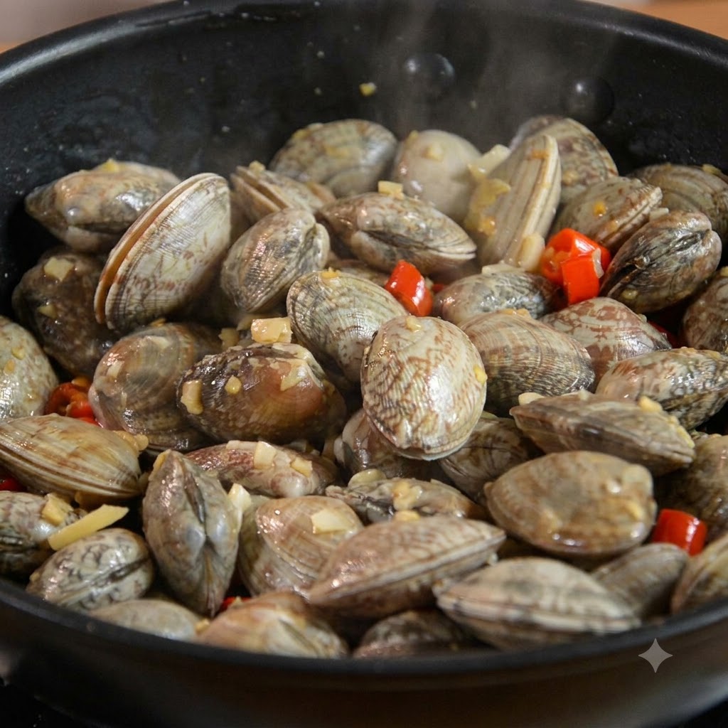 Almejas mezcladas con ajo y chile dentro de una sartén negra.