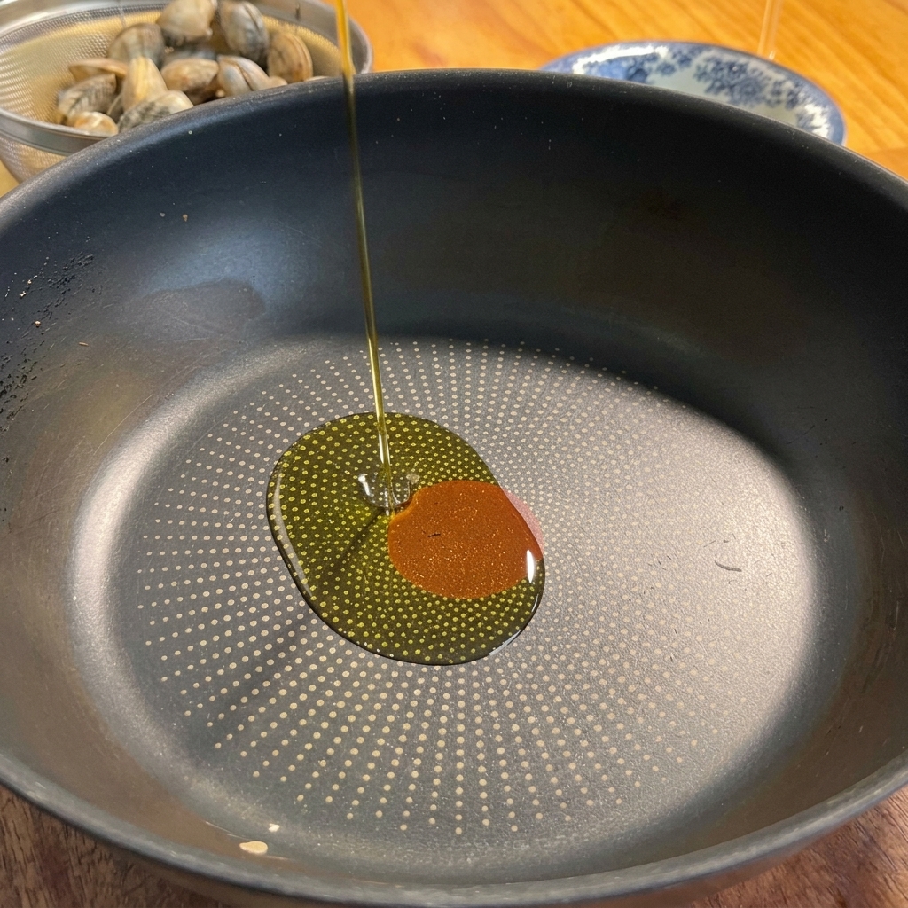 Aceite de oliva siendo vertido en una sartén junto con ajo y chile rojo.