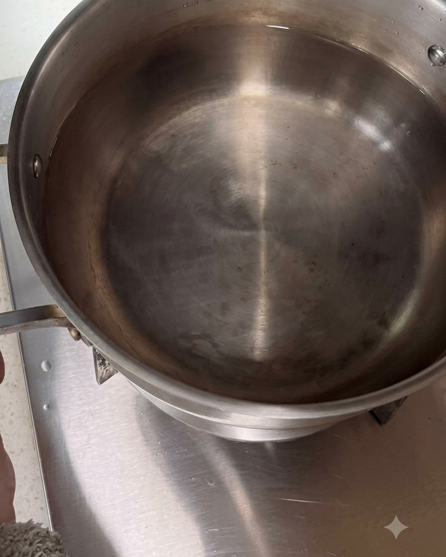 Olla de acero inoxidable llena de agua colocada en el quemador de una estufa.