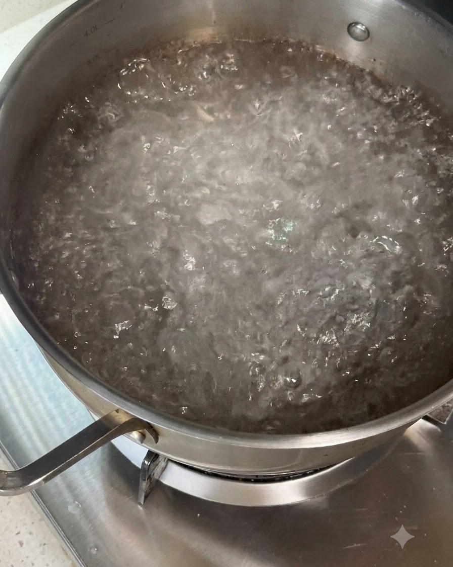 Pasta seca siendo revuelta en una olla de agua hirviendo usando utensilios.