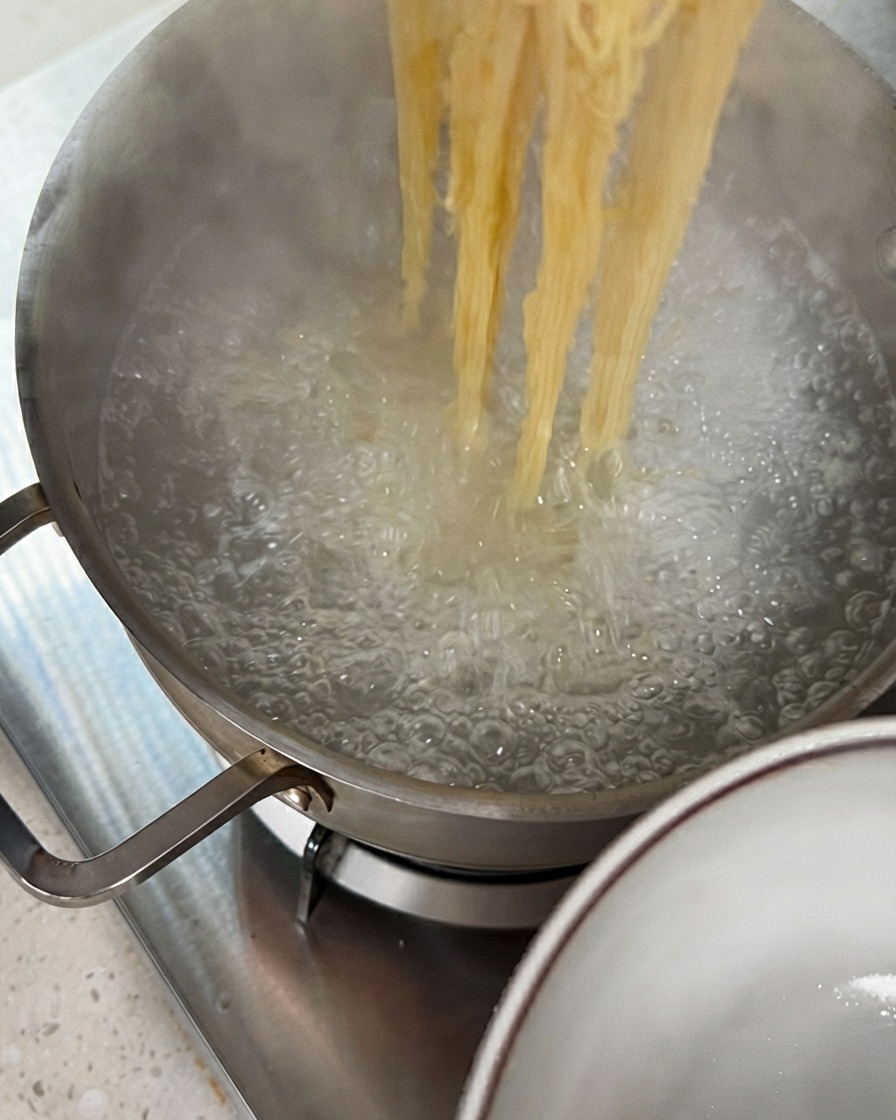 Pinzas levantando hebras de fideos cocidos de una olla de agua hirviendo.