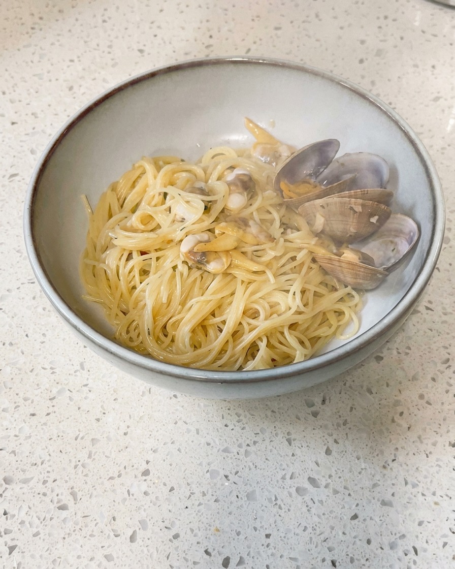 Pequeños trozos de mantequilla fría siendo arrojados a una sartén que contiene almejas cocidas y caldo.