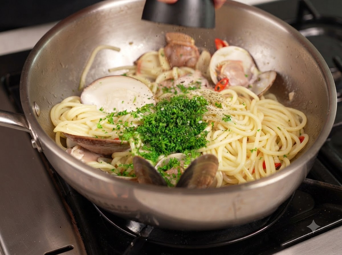 Pimienta negra siendo molida desde un molinillo sobre una sartén de pasta y almejas cubierta con perejil verde picado.