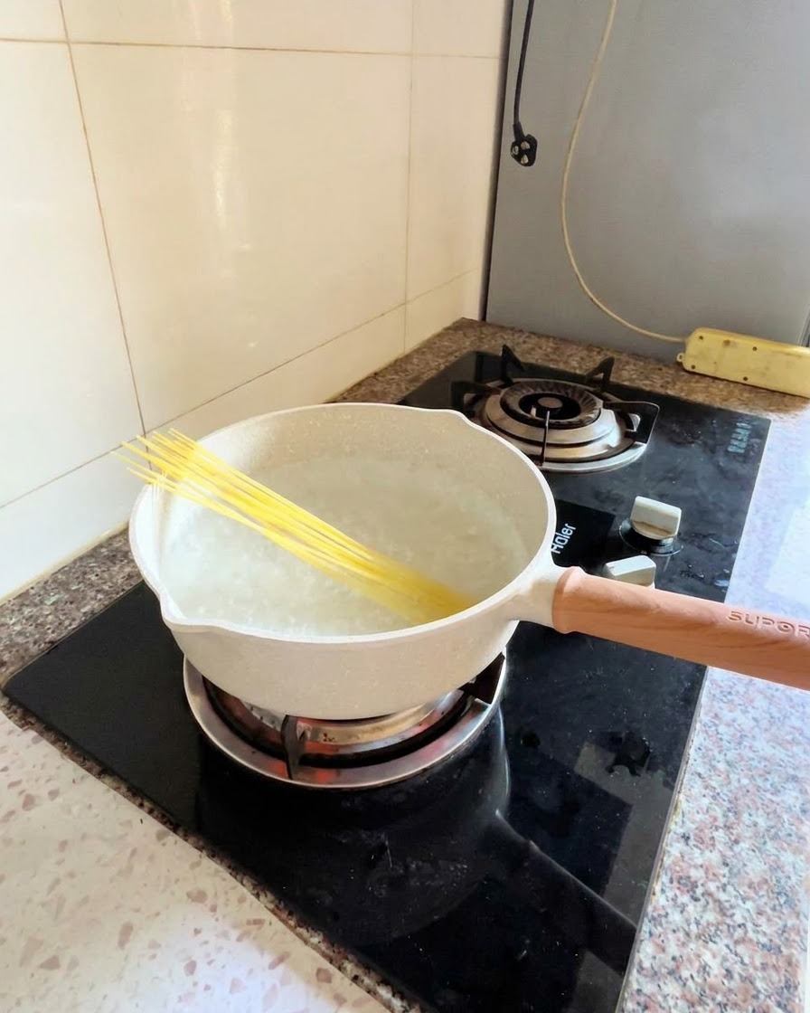 Fideos de espagueti seco colocados en diagonal en una olla con agua hirviendo sobre una estufa.
