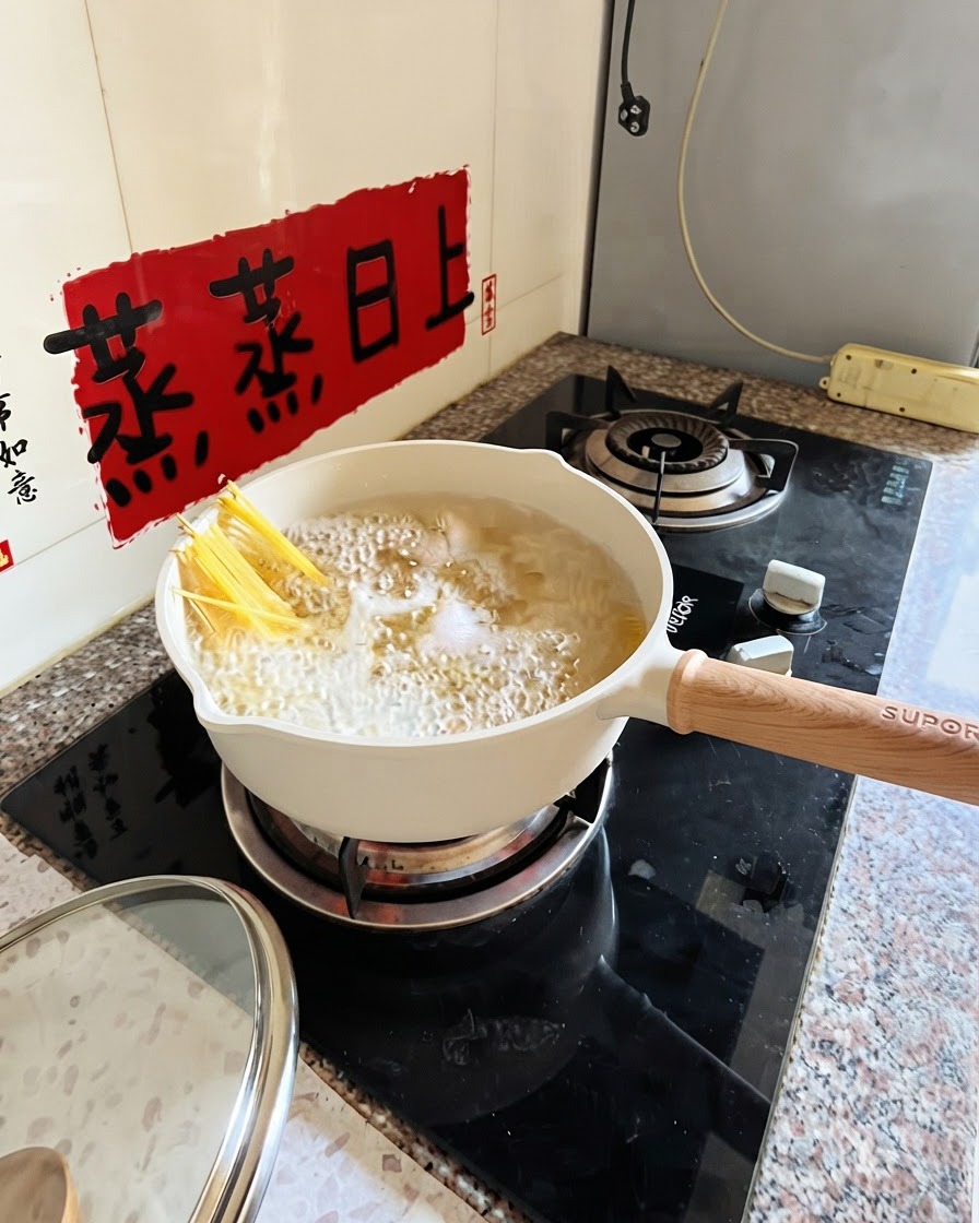 Espaguetis hirviendo en una olla blanca con pinzas sumergiendo parcialmente los fideos.