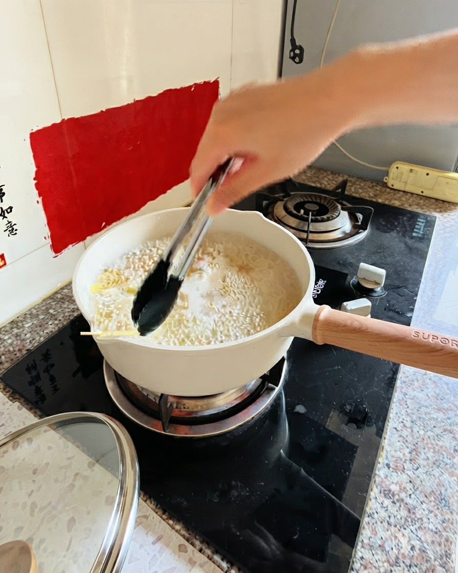 Pinzas removiendo pasta en una olla con agua hirviendo en la estufa.