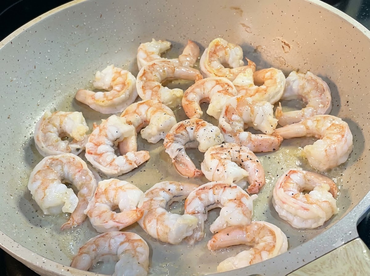 Camarones friéndose en una sartén con pimienta negra espolvoreada por encima.
