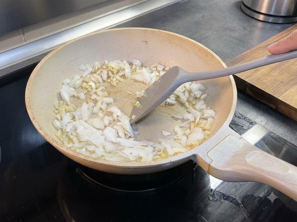 Cebollas picadas siendo revueltas con mantequilla derretida dentro de una sartén usando una espátula.