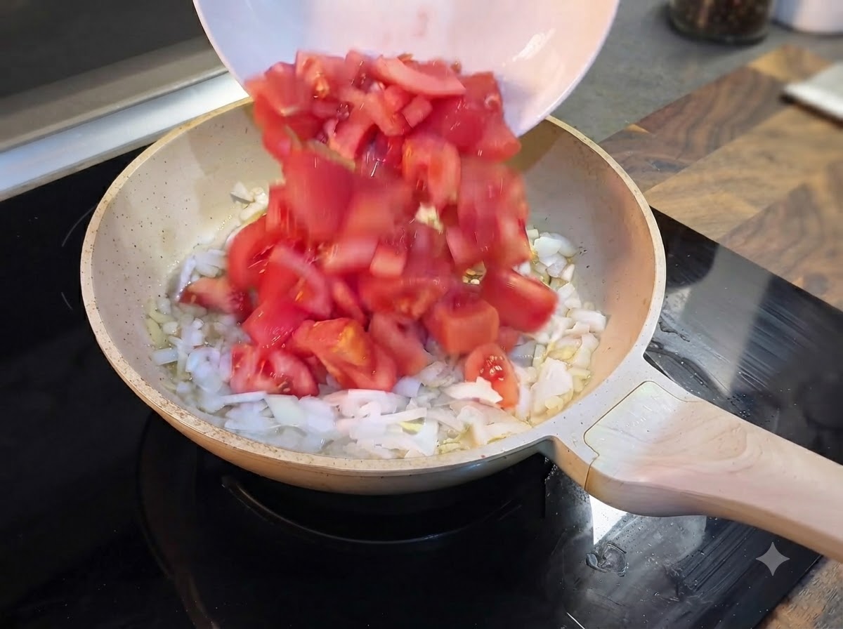 Tomates rojos recién picados siendo vertidos desde un tazón blanco a la sartén con cebollas.