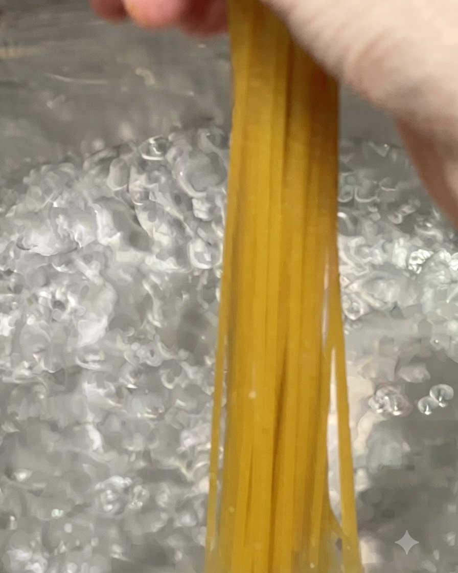 Fideos de pasta espagueti siendo sumergidos en una olla grande con agua hirviendo burbujeante.