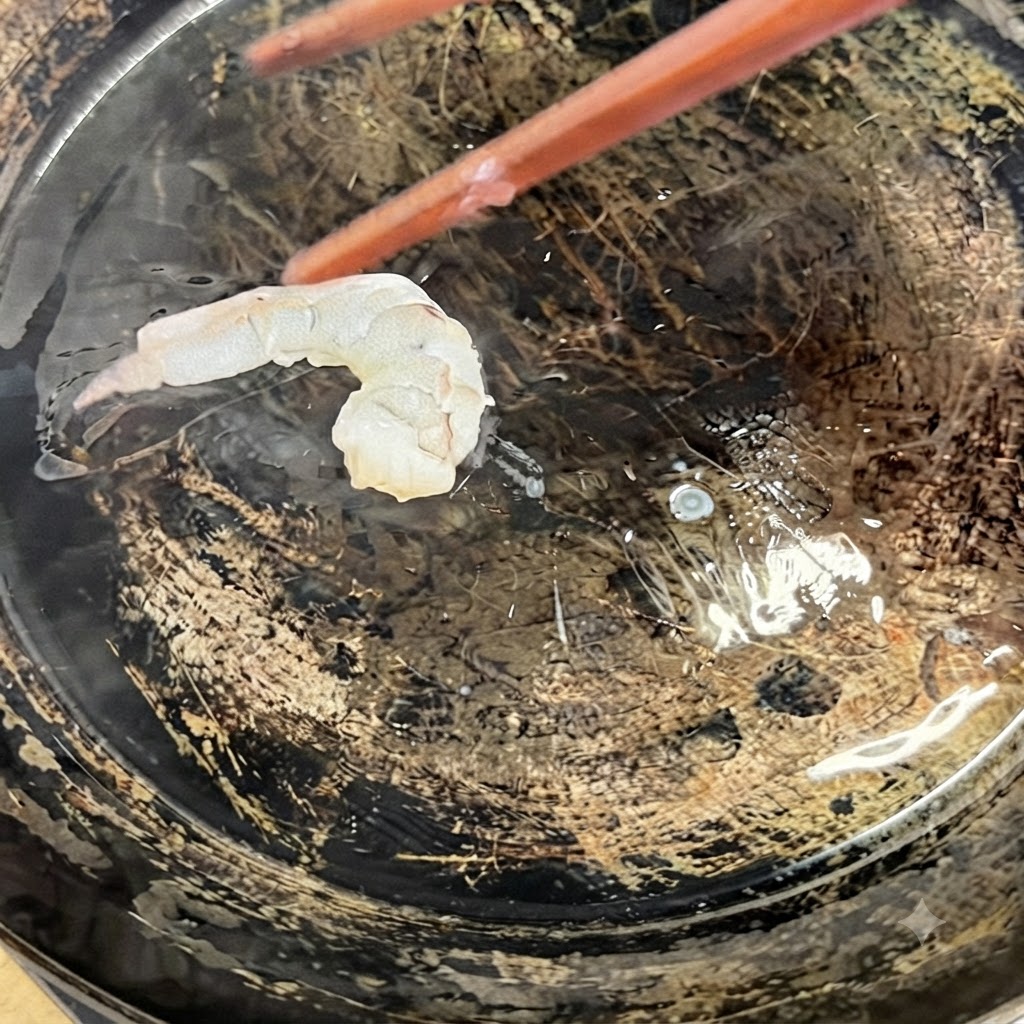 Camarones en mariposa siendo colocados en una sartén caliente con aceite usando palillos de cocina.
