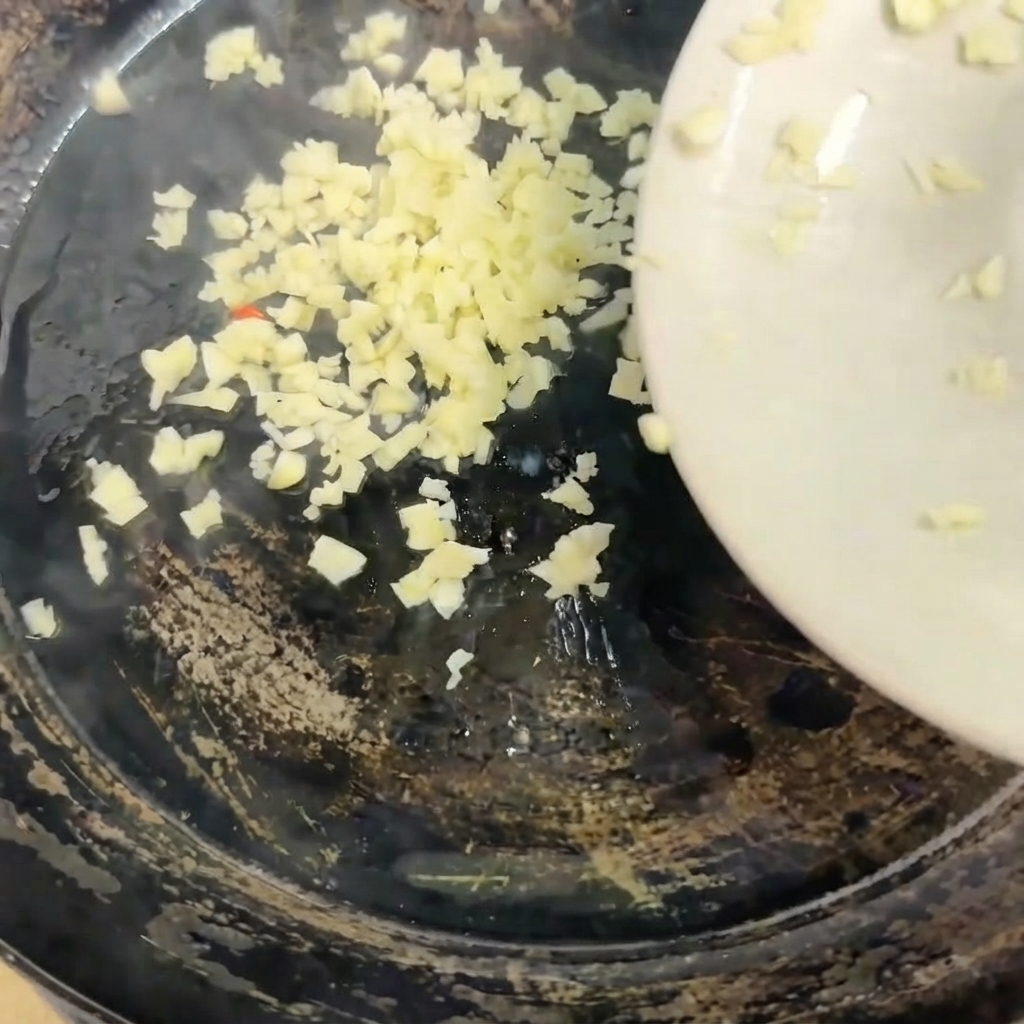 Ajo picado siendo vertido desde un plato blanco hacia una sartén caliente.