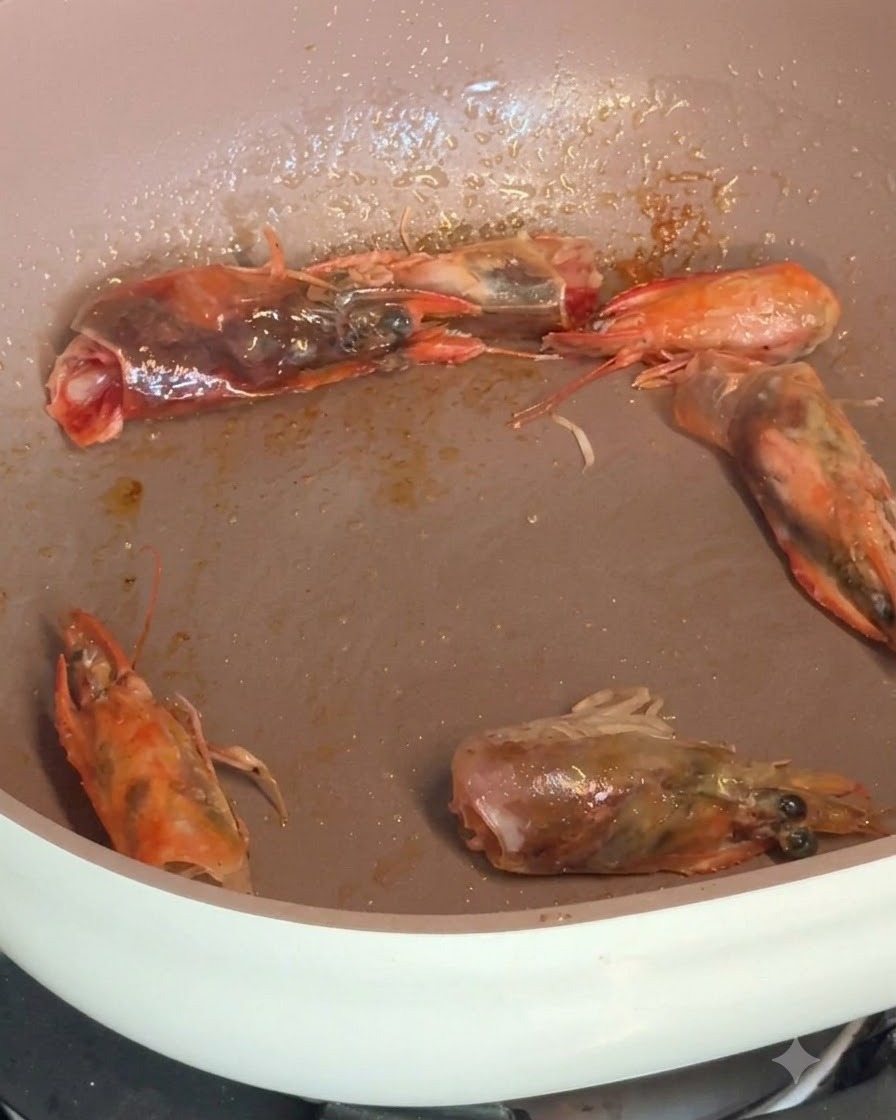 Camarones pelados y cabezas de camarón chisporroteando en una sartén mientras se sazonan con especias.