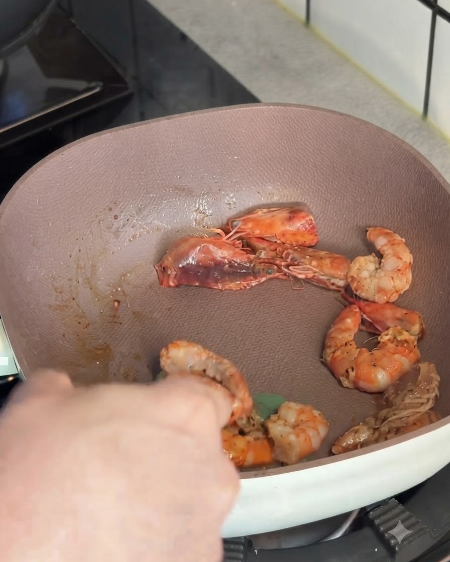 Camarones rosados salteados siendo levantados de una sartén poco profunda con un utensilio de cocina.