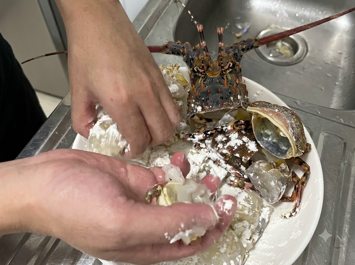 Manos mezclando activamente trozos de carne y caparazón de langosta cruda con maicena blanca en un plato para asegurar un rebozado uniforme.