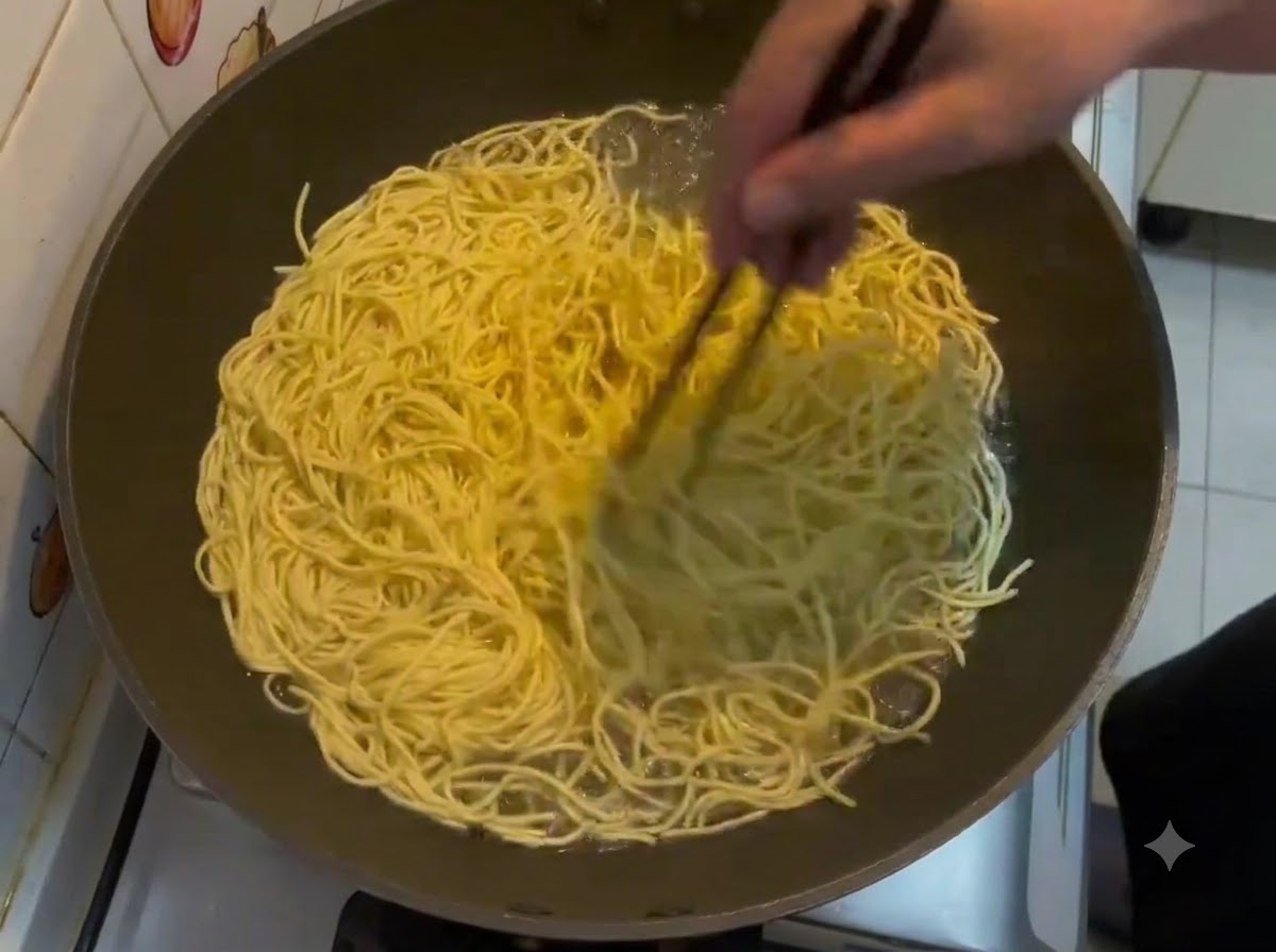 Palillos removiendo una gran cantidad de fideos amarillos E-fu hirviendo en un wok.