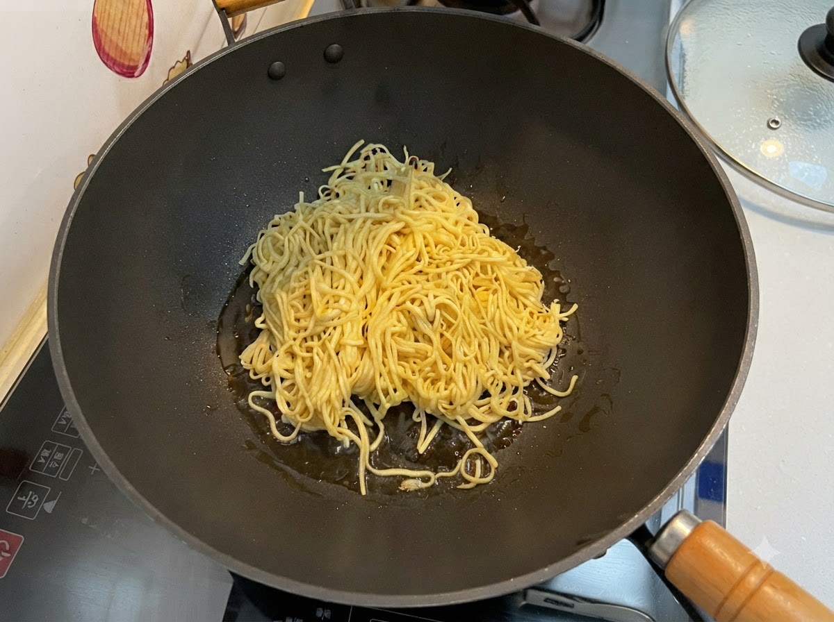 Fideos E-fu escurridos siendo salteados en un wok negro con la ayuda de una espátula.