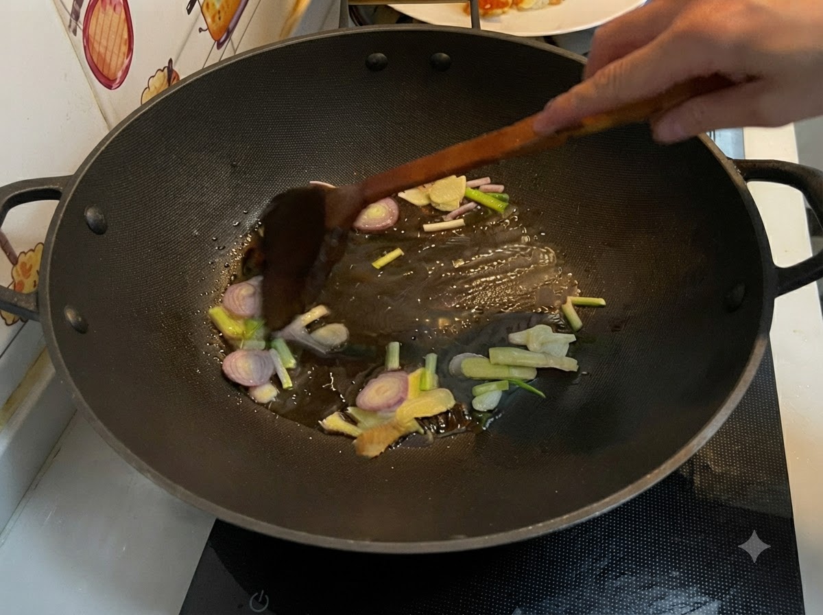 Rodajas de jengibre, ajo, chalota y cebolleta friéndose en aceite caliente dentro de un wok, siendo removidos con una espátula de madera.