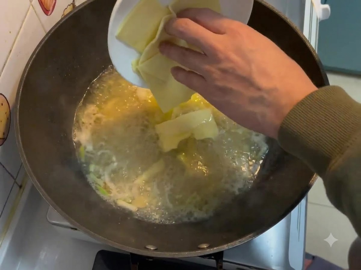 Lonchas de queso cuadradas cayendo desde un plato blanco a un caldo cremoso burbujeante en un wok.