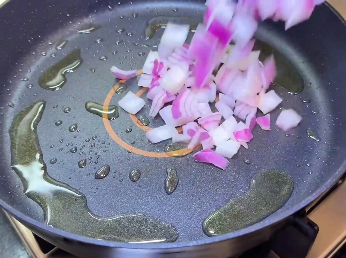 Cebollas moradas picadas cayendo en una sartén con aceite.
