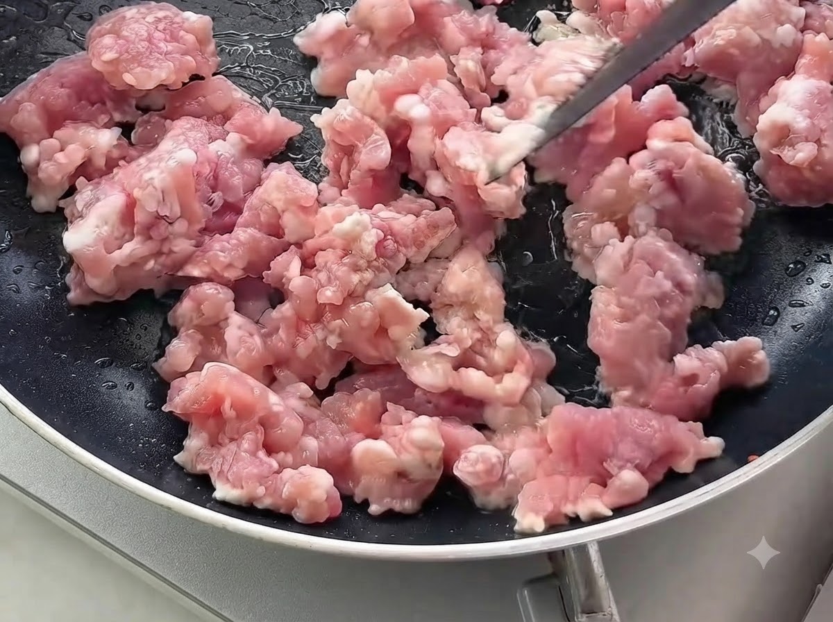 Carne de cerdo picada cruda siendo removida y cocinada en una sartén negra.