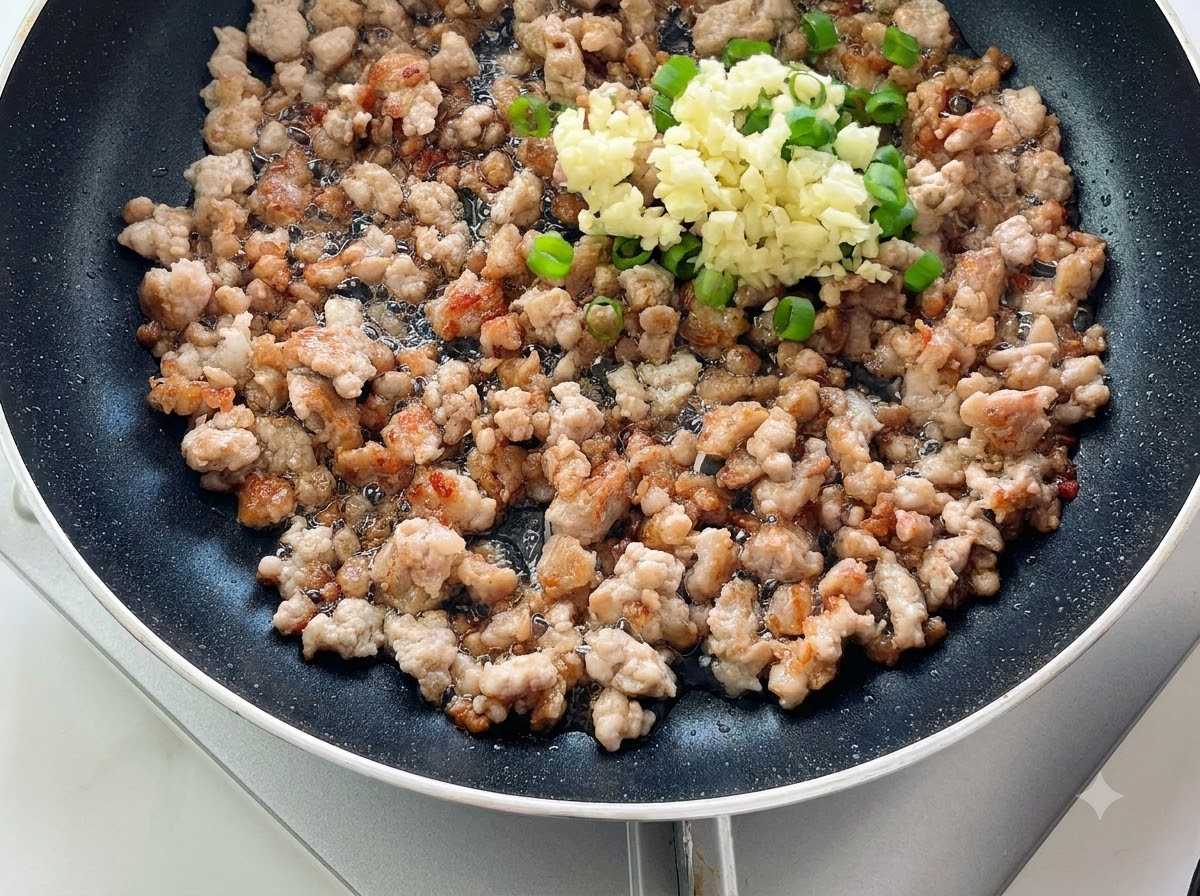 Ajo picado y cebollas verdes amontonados sobre carne picada cocida en una sartén.