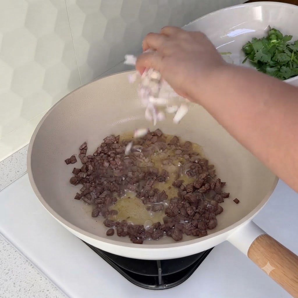 Cebollas en dados siendo esparcidas en un wok que contiene carne picada de ternera cocinada.