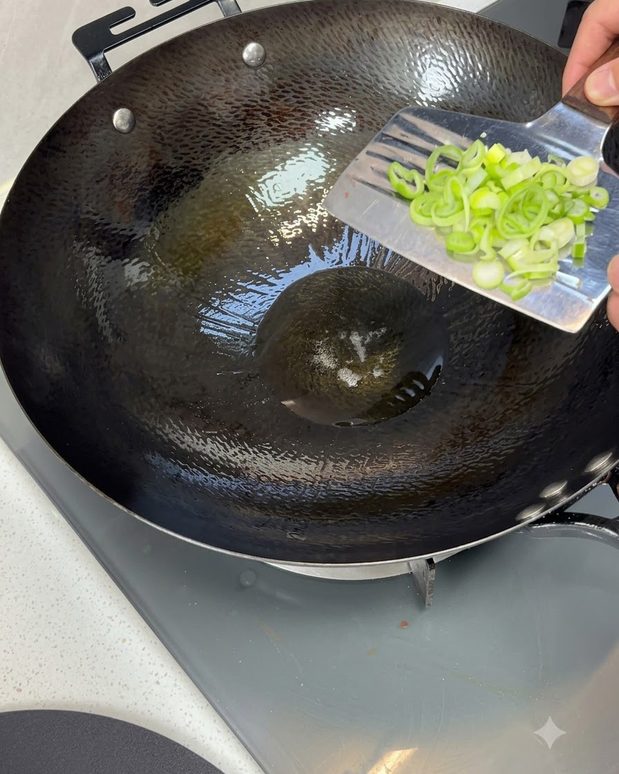 Cebolletas picadas cayendo en un wok caliente lleno de aceite de cocina brillante.