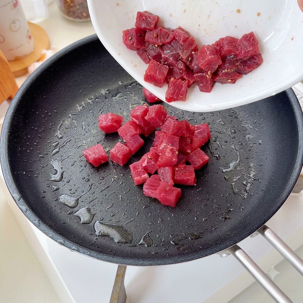 Cubos de carne sazonados siendo vertidos y salteados en una sartén.