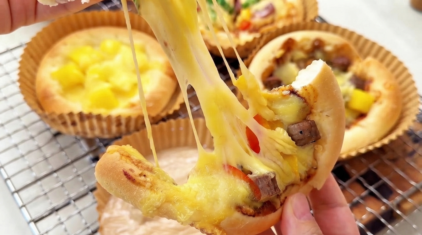 Una mini pizza casera recién horneada con un estiramiento de queso dramático, cubierta con salchicha y pimientos coloridos.