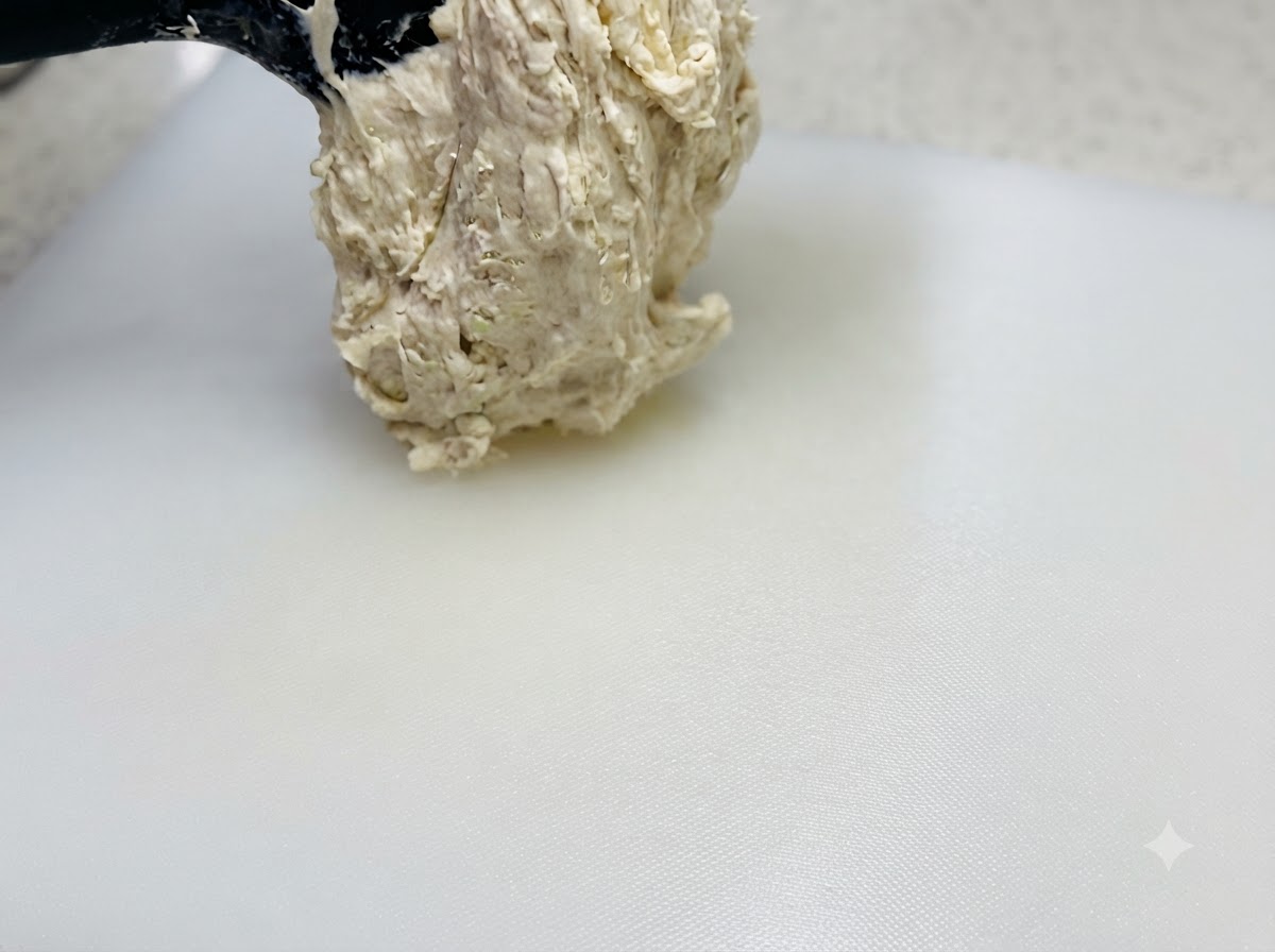 Masa pegajosa de alta hidratación que se levanta con una espátula y se coloca sobre una tabla de cortar blanca rociada con aceite.
