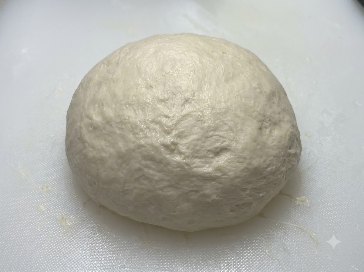 Una bola de masa lisa y redondeada que reposa sobre una tabla blanca antes de ser cubierta.