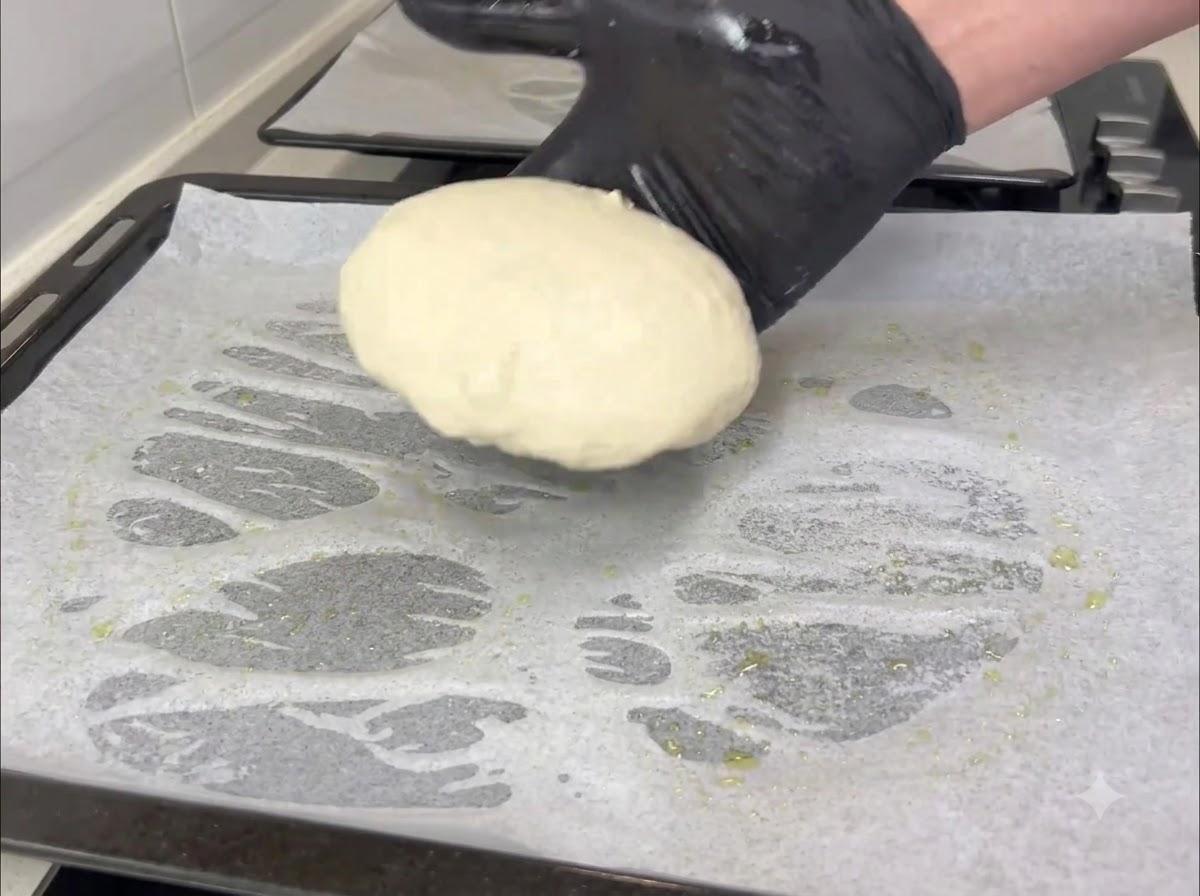 Una mano enguantada transfiere una pequeña porción redonda de masa a una bandeja forrada con papel de horno.