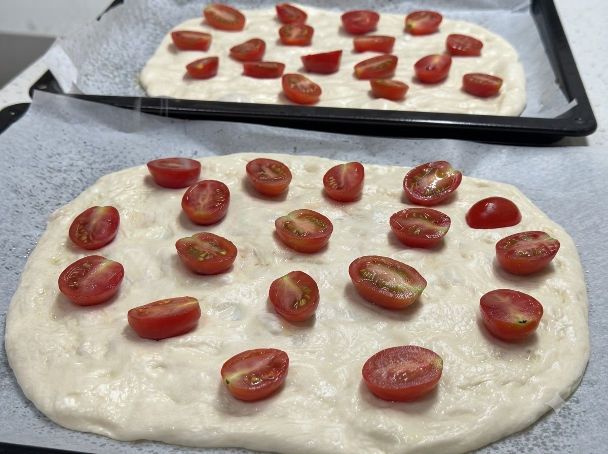 Primer plano de dos bases de masa de pizza estiradas cubiertas con mitades de tomates cherry, listas para condimentar.