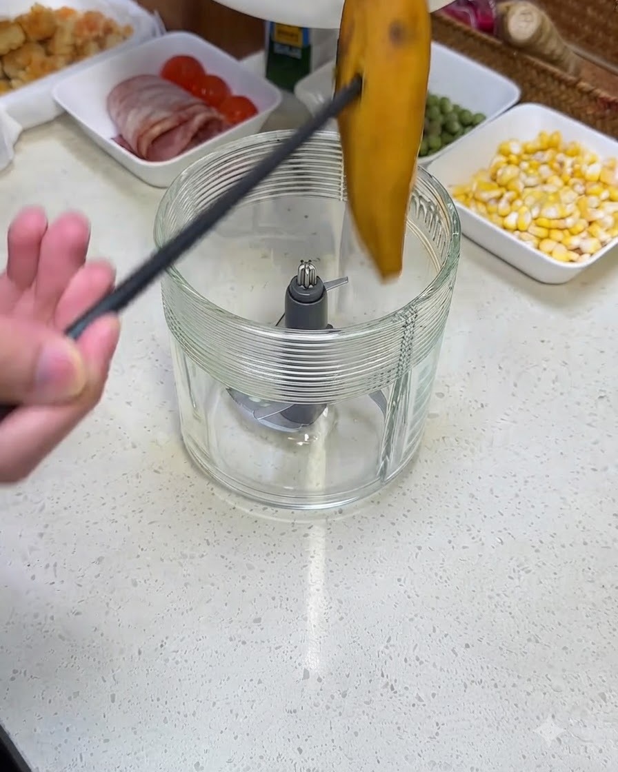 Una persona usando pinzas negras para colocar un trozo de batata cocida en un vaso de licuadora de vidrio.